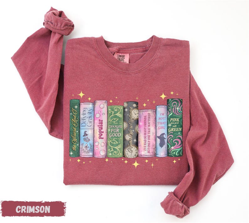 A red long-sleeved t-shirt with a graphic design of a row of colorful books with stars on the cover.