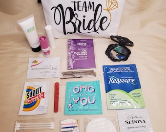 May include: A white zippered pouch with the text "TEAM Bride" and a gold ring design. The pouch is filled with various items, including makeup remover wipes, nail polish remover pads, cotton swabs, bandages, and a small mirror.