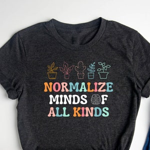 May include: A dark grey t-shirt with a graphic design of potted plants and the text "Normalize Minds of All Kinds".
