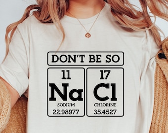 May include: White t-shirt with a black graphic of the chemical formula for sodium chloride (NaCl) with the text "Don't be so Na Cl".
