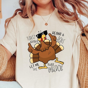 May include: A white t-shirt with a cartoon turkey wearing sunglasses and the text "Turkey Gravy Let Me See That Casserole Beans & Rolls".