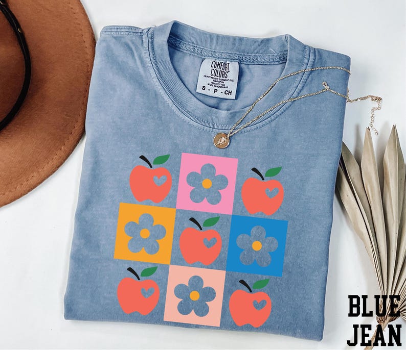 a blue t-shirt with a colorful graphic design of apples and flowers, along with a necklace and a hat.