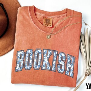 a red t-shirt with the word "BOOKISH" printed on it, along with a brown hat and a fan.