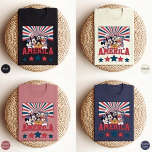 May include: Four t-shirts with a vintage-style graphic of Mickey Mouse, Minnie Mouse, Donald Duck, and Goofy in front of a red, white, and blue American flag with the word "AMERICA" printed below. The t-shirts are available in black, natural, heather mauve, and heather navy.