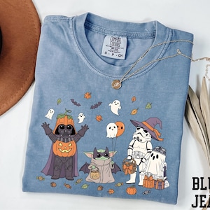 A blue t-shirt with a Halloween-themed graphic design featuring characters from the Star Wars franchise, including Darth Vader, Baby Yoda, Stormtrooper, and other iconic figures.