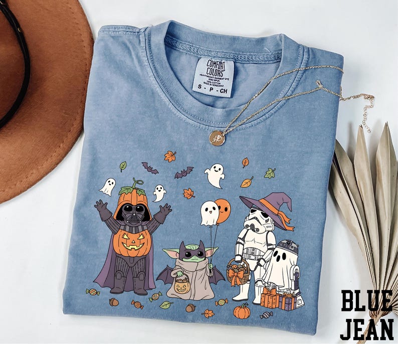 A blue t-shirt with a Halloween-themed graphic design featuring characters from the Star Wars franchise, including Darth Vader, Baby Yoda, Stormtrooper, and other iconic figures.