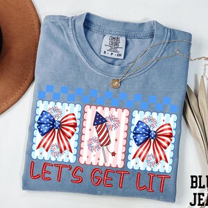 A blue t-shirt with a patriotic design, including fireworks and American flags, along with the text "Let's Get Lit" printed on it.