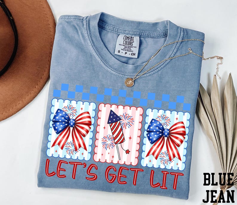 A blue t-shirt with a patriotic design, including fireworks and American flags, along with the text "Let's Get Lit" printed on it.