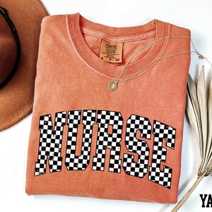 a red t-shirt with the word "NURSE" printed on it, along with a brown hat and a fan.