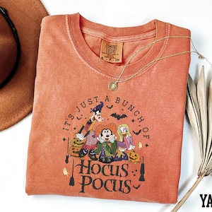A red t-shirt with a Halloween-themed graphic design, including characters from the Disney movie Hocus Pocus, along with the text "It's just a bunch of Hocus Pocus".