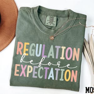 May include: A green t-shirt with the text "REGULATION before EXPECTATION" in rainbow colours.