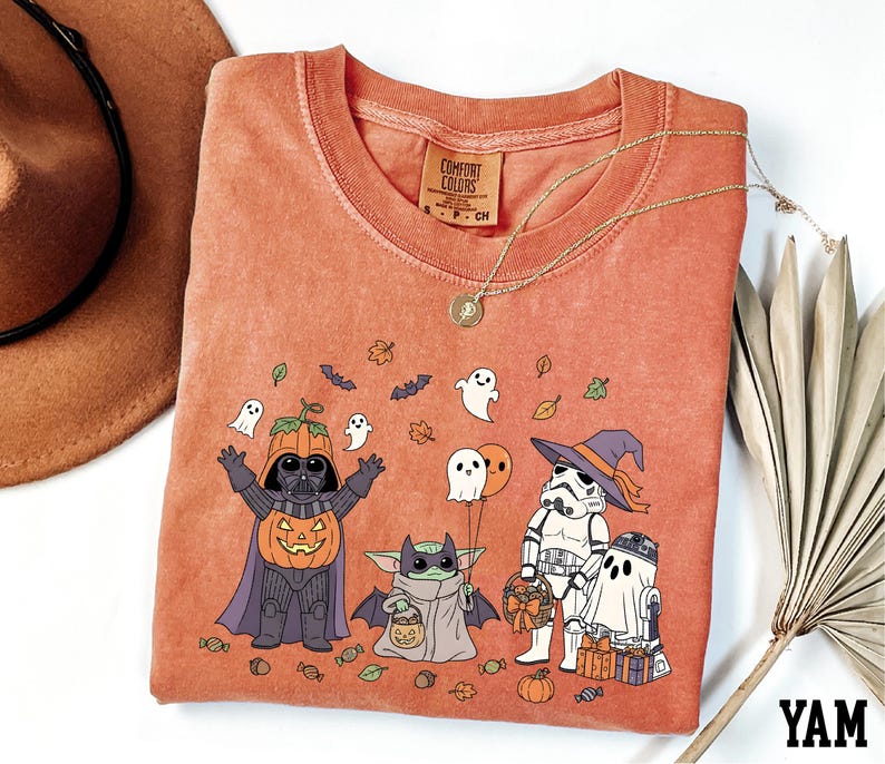 a Halloween-themed t-shirt with a design of various characters, including Darth Vader, Baby Yoda, Stormtrooper, and Ghost Batter, along with Halloween-related elements such as pumpkins, bats, and leaves.