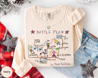 May include: Ivory long-sleeved t-shirt featuring a hand-drawn "BATTLE PLAN" graphic. The design includes text and illustrations of various items like "heavy cans", "ice", and "fire". The text "by Kevin McCallister" is also included.
