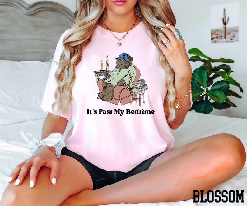 a woman sitting on a bed wearing a pink shirt