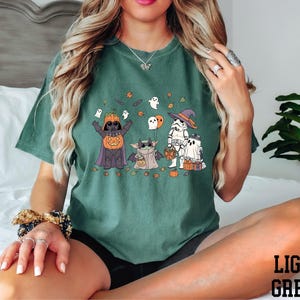 A woman wearing a green t-shirt with a Halloween-themed graphic of characters such as Darth Vader, a pumpkin, and a ghost.