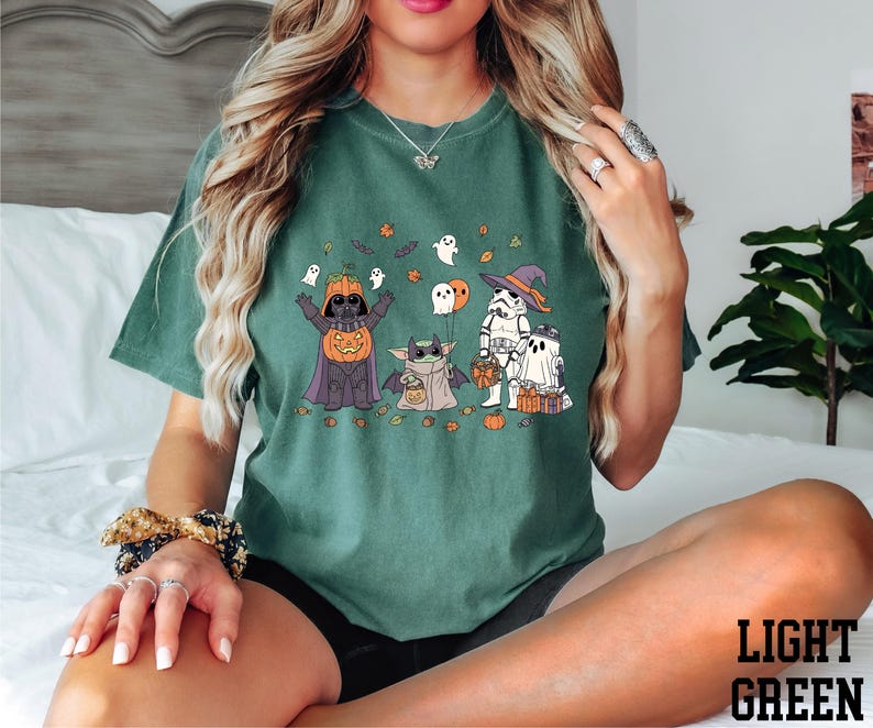 A woman wearing a green t-shirt with a Halloween-themed graphic of characters such as Darth Vader, a pumpkin, and a ghost.
