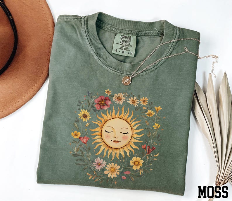 a green t-shirt with a sun design, a brown hat, and a necklace, all placed on a white surface.