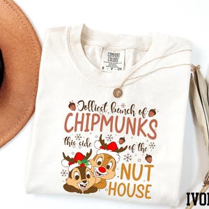 Peut inclure: T-shirt ivoire avec l'inscription "Jolliest bunch of Chipmunks" et un dessin de Chip et Dale portant des bonnets de Père Noël. L'expression "of the Nut House" est également imprimée.