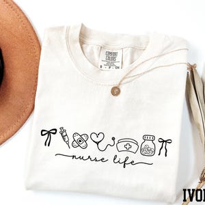 a white t-shirt with a graphic design, a brown hat, a necklace, and some dried leaves, all arranged on a white background.