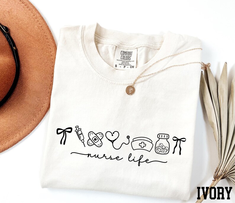 a white t-shirt with a graphic design, a brown hat, a necklace, and some dried leaves, all arranged on a white background.