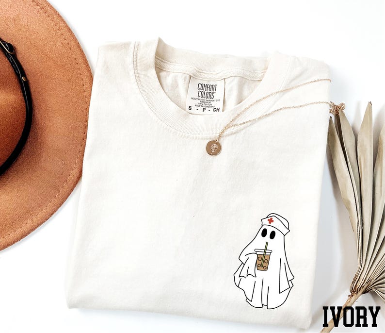 a white t-shirt with a graphic of a ghost wearing a nurse's hat and holding a drink, along with a necklace and a brown hat.