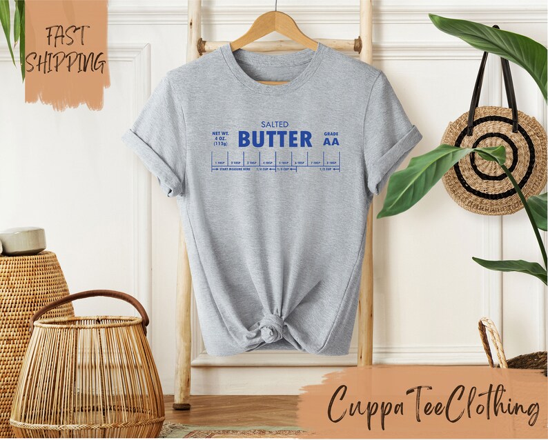 Puede incluir: Camiseta gris con un gr&aacute;fico azul de una etiqueta de mantequilla que dice "Salted Butter Grade AA" e incluye una tabla para medir la mantequilla en cucharadas y tazas.