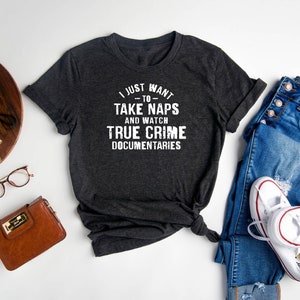 May include: A dark gray t-shirt with the text "I just want to take naps and watch true crime documentaries" printed in white.