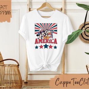 May include: White t-shirt with a red, white, and blue graphic of Mickey Mouse and friends with the word "AMERICA" and stars.