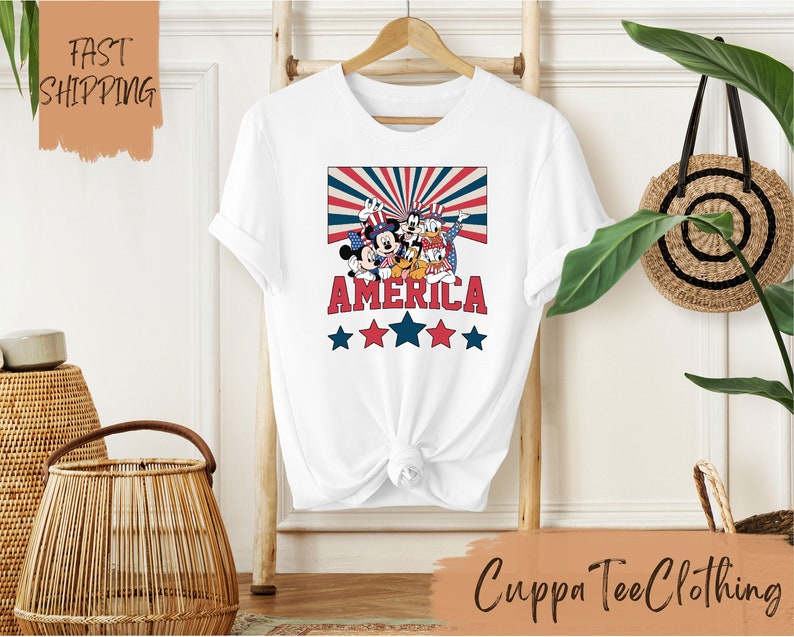 May include: White t-shirt with a red, white, and blue graphic of Mickey Mouse and friends with the word "AMERICA" and stars.