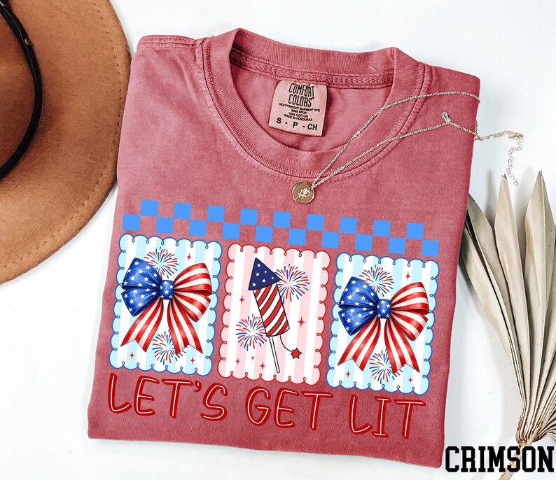 a red t-shirt with a patriotic design, including American flags and fireworks, along with the text "Let's Get Lit" printed on it.