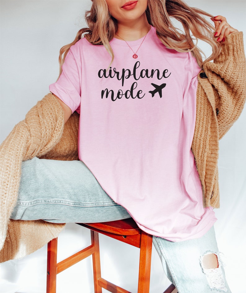 Puede incluir: Una camiseta rosa con el texto "airplane mode" y un peque&ntilde;o avi&oacute;n impreso en la parte delantera.