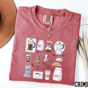 a red t-shirt with a graphic design of various coffee-related items, such as a coffee maker, coffee cup, and coffee beans, along with the text "Coffee Club".