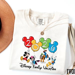 A white t-shirt with a colorful graphic design featuring Disney characters and balloons, along with the text "Disney Family Vacation".