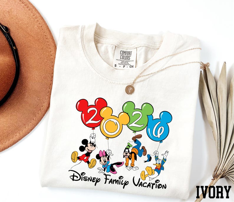A white t-shirt with a colorful graphic design featuring Disney characters and balloons, along with the text "Disney Family Vacation".