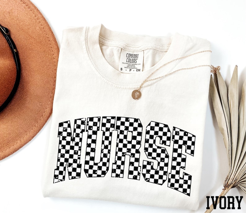 a white t-shirt with the word "NURSE" printed in black and white checkered letters, along with a brown hat and a necklace.