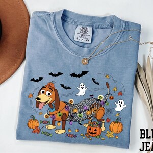 A blue t-shirt with a Halloween-themed design, including a cartoon dog, bats, a ghost, and pumpkins, along with a necklace and a hat.