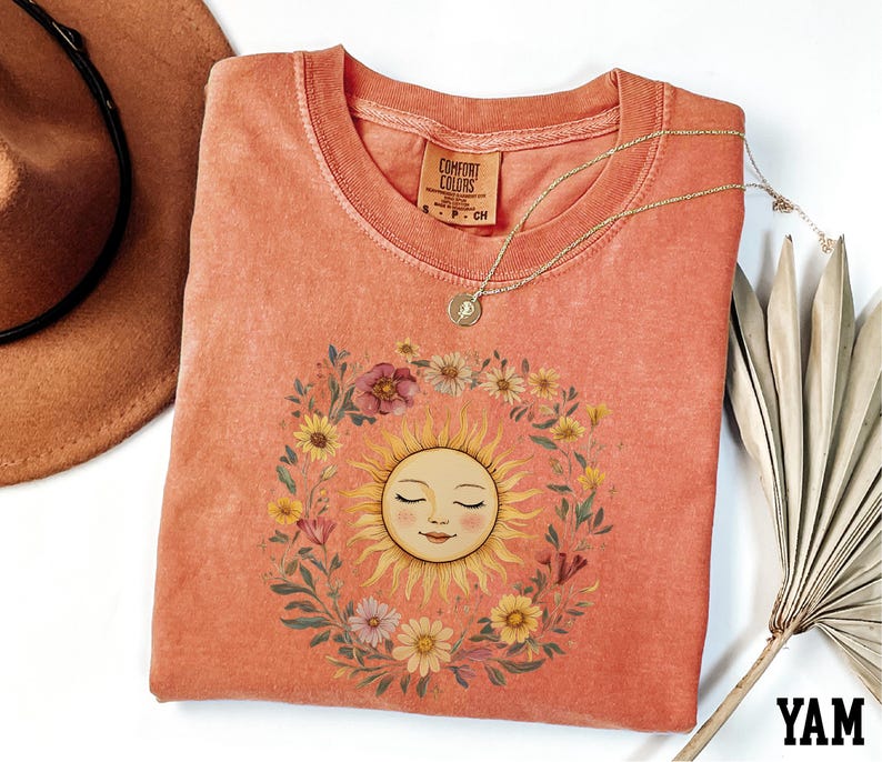 a pink t-shirt with a sun design, a brown hat, and a necklace, all arranged on a white background.