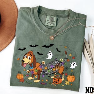 a green t-shirt with a Halloween-themed design, including a cartoon dog, bats, a ghost, pumpkins, and candy canes.