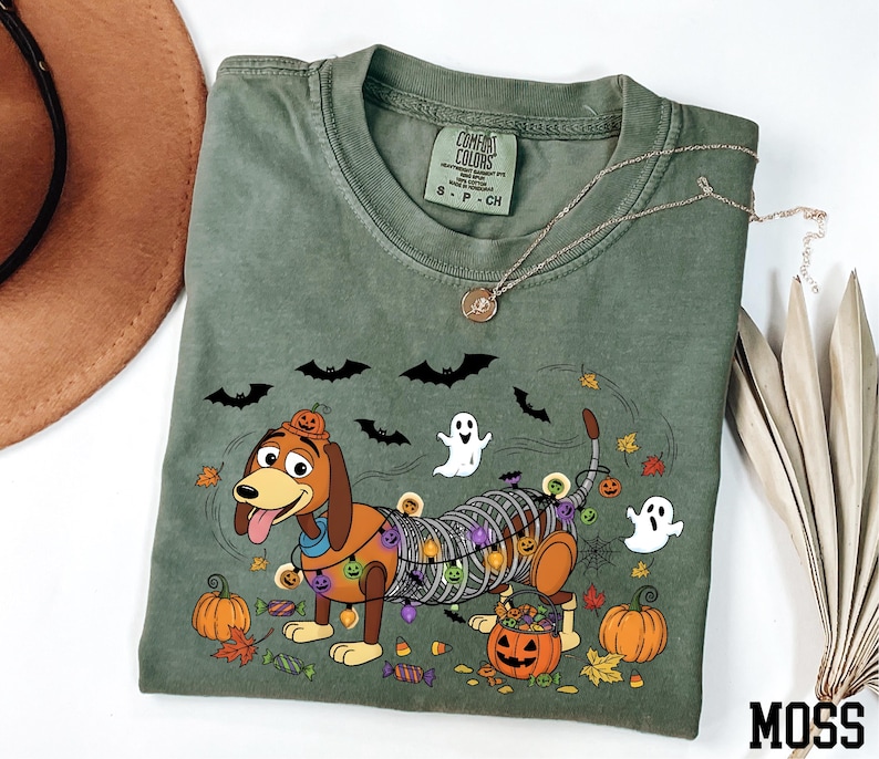 a green t-shirt with a Halloween-themed design, including a cartoon dog, bats, a ghost, pumpkins, and candy canes.
