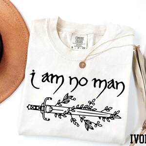 a t - shirt that says i am no man next to a hat