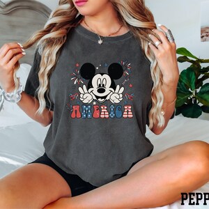 a woman sitting on a bed wearing a mickey mouse shirt