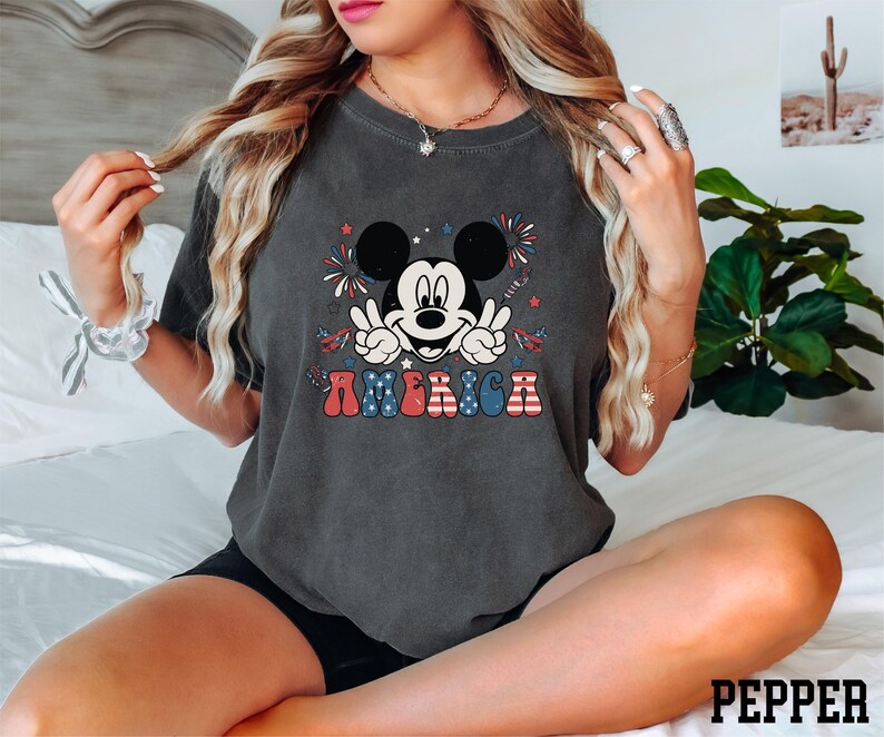 a woman sitting on a bed wearing a mickey mouse shirt