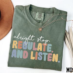 May include: A green t-shirt with the text "alright stop. REGULATE. AND LISTEN." in rainbow colors.
