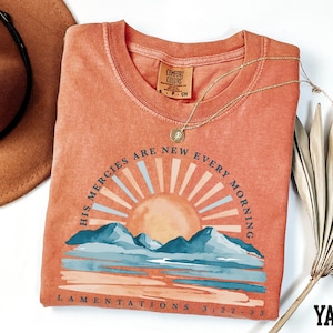 a t - shirt with a sunset on it next to a hat