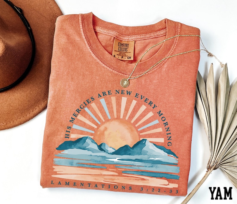 a t - shirt with a sunset on it next to a hat