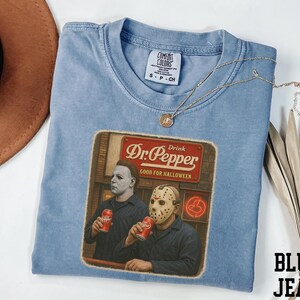 A blue t-shirt with a graphic design featuring two men dressed in Halloween costumes, one wearing a mask and the other holding a can of Dr. Pepper, along with a sign that says "Dr Pepper".