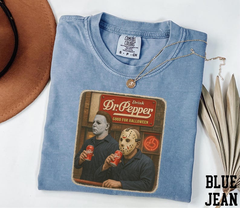 A blue t-shirt with a graphic design featuring two men dressed in Halloween costumes, one wearing a mask and the other holding a can of Dr. Pepper, along with a sign that says "Dr Pepper".