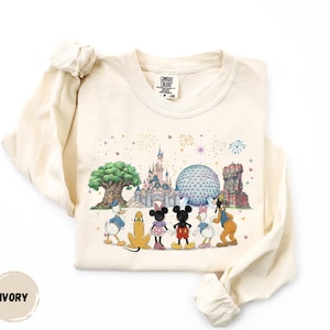 A white long-sleeved t-shirt with a printed design featuring Disney characters and landmarks, including Mickey Mouse, Donald Duck, Goofy, and the Space Needle.