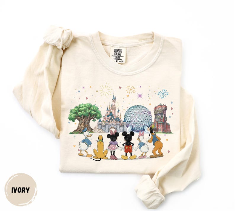 A white long-sleeved t-shirt with a printed design featuring Disney characters and landmarks, including Mickey Mouse, Donald Duck, Goofy, and the Space Needle.