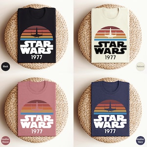 May include: Four folded t-shirts with a retro-style Star Wars graphic featuring a spaceship and the text "STAR WARS 1977". The shirts are shown in black, natural, heather mauve, and heather navy.